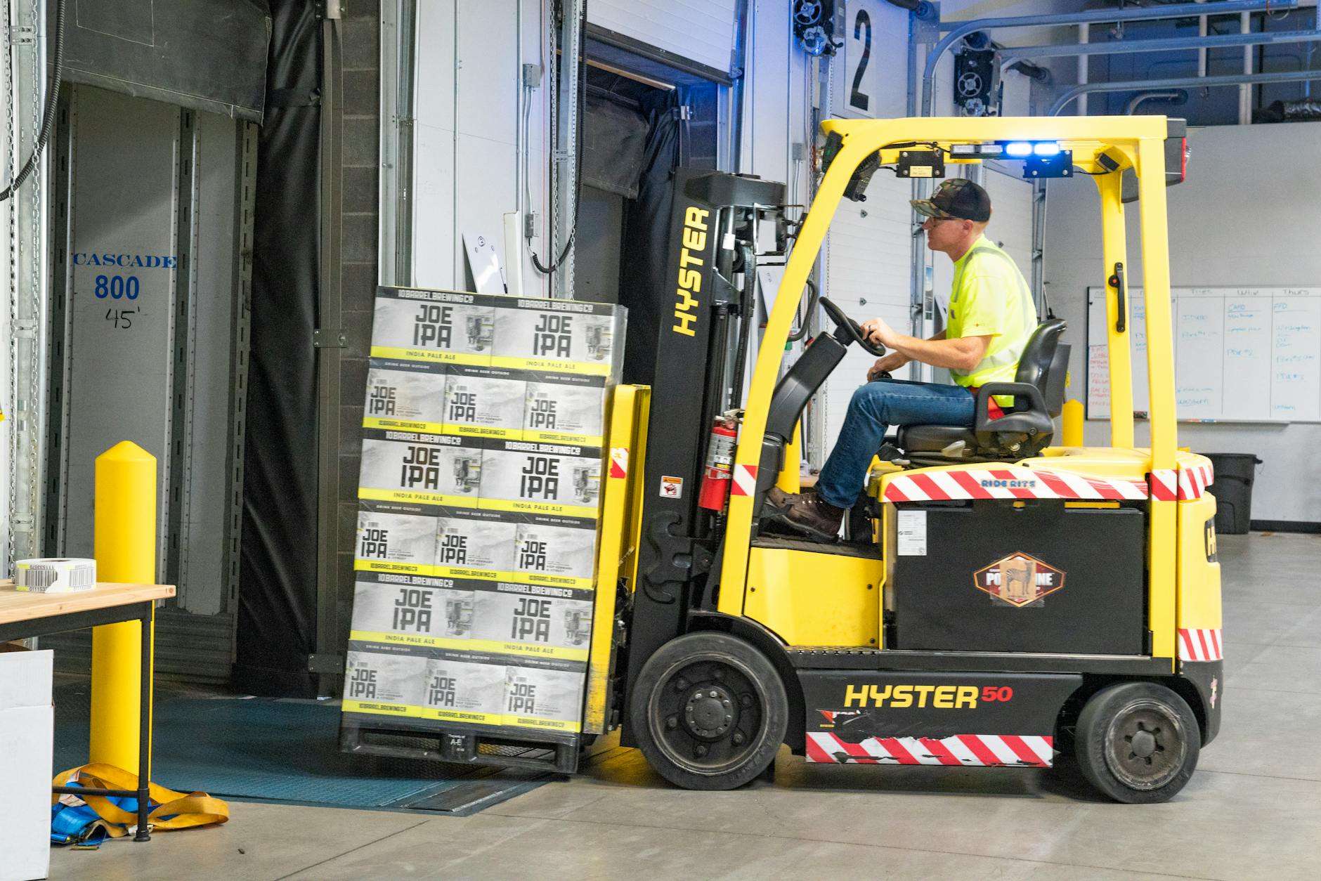 man riding a yellow forklift lifting boxes case picking